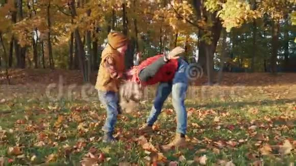 母亲和蹒跚学步的儿子正在秋天的公园或森林里和落叶一起玩耍妈妈把树叶扔进去视频的预览图