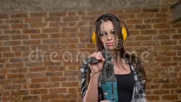 戴着眼镜戴着耳机戴着电钻看着相机的漂亮漂亮年轻女性女建筑工人砖头视频的预览图