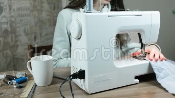 女人在缝纫机上缝制浅色织物在桌子上喝杯茶视频的预览图