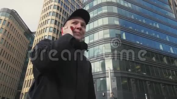 戴着黑帽子的男人在城市街头散步时用手机说话视频的预览图