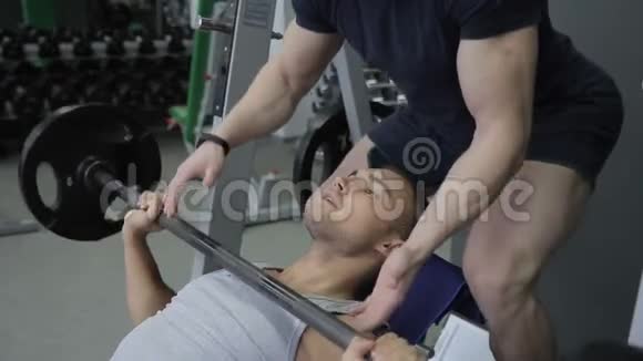 年轻的运动员正和他的教练一起在健身房做他在斜凳上的努力视频的预览图