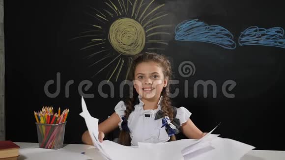 学校观念漂亮的女孩坐在书桌前身后有一块黑板快乐的女学生扔纸微笑视频的预览图