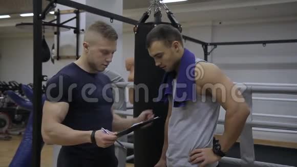 年轻的运动员正在讨论他的教练在健身房的训练结果视频的预览图