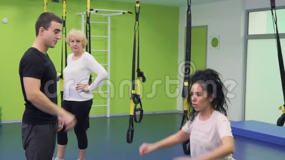教练帮助年轻女子正确地蹲在健身房里视频的预览图