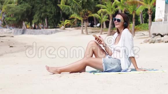 一个年轻的女人在阳光明媚的日子里在海滩上听音乐视频的预览图
