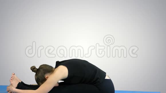 年轻女子在垫子上伸腿在白色背景下练习瑜伽视频的预览图