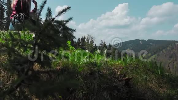 一个年轻的高加索女人带着背包坐在山顶上的一根木头上戴着一顶帽子的概念视频的预览图