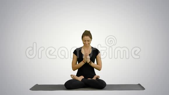年轻女子练习瑜伽坐在莲花的位置闭着眼睛在白色的背景上沉思视频的预览图