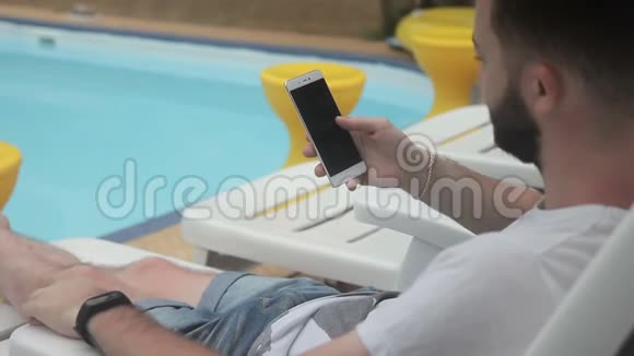 男性旅行者的肖像他正在检查他的社交网络同时在游泳池附近休息视频的预览图