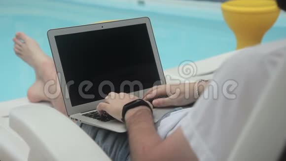 酒店的访客通过泳池在笔记本电脑上写博客评论视频的预览图