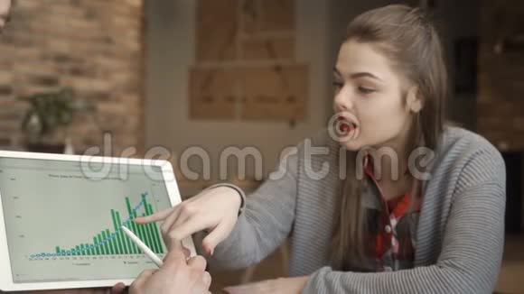 两位年轻的商人在看数字平板电脑时讨论货币增长率视频的预览图