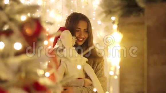 手里拿着格子呢和圣诞老人的年轻女子微笑着走到圣诞树旁边视频的预览图