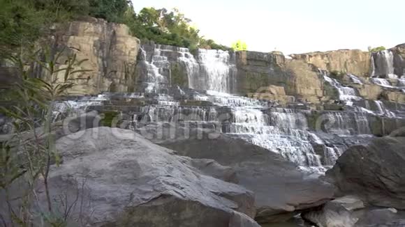 女人爬在岩石上举起双手站在达拉特的Pongour瀑布附近视频的预览图