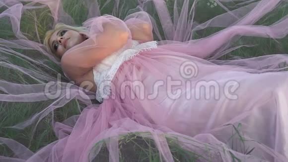 穿着粉红色裙子躺在草地上的漂亮年轻女子视频的预览图