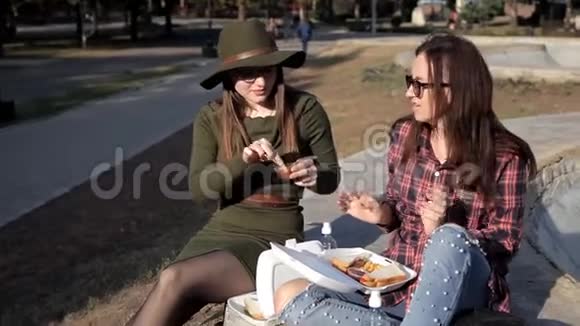 秋天女孩们坐在公园里她们吃薯条和三明治交流视频的预览图