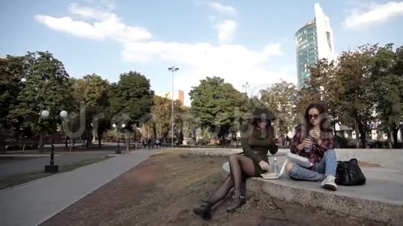 年轻的女孩坐在公园里吃三明治喝水散步吃饭视频的预览图