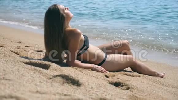 穿比基尼的年轻女孩躺在海边和日光浴美丽的白种人女性夏天在海边放松视频的预览图