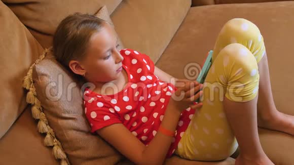 年轻女孩坐在沙发上在舒适的客厅里浏览手机视频的预览图