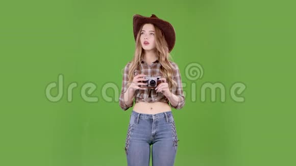 戴着帽子牛仔靴和背心的女孩手里拿着相机绿色屏幕视频的预览图