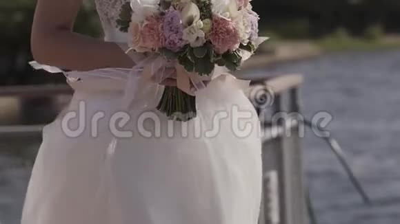 一个迷人的新娘的中倾手里拿着一个精致的婚纱站在湖边在远处眺望视频的预览图