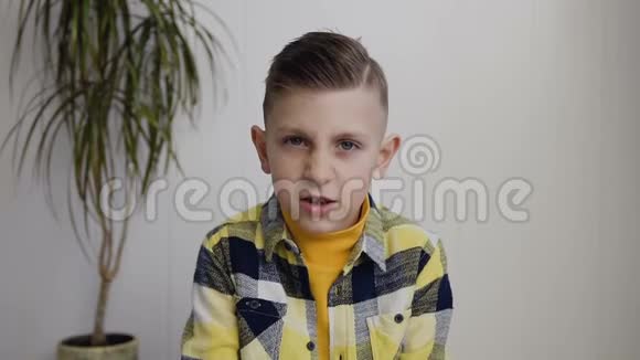 一幅美丽的七岁八岁男孩的肖像他坐在白色墙壁背景上的地板上孩子生气的脸视频的预览图
