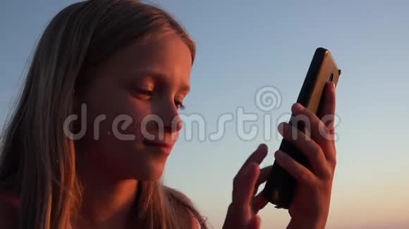 孩子在玩智能手机日落时在海滩上玩女孩在玩平板电脑视频的预览图