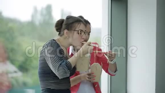 两个漂亮的女商人站在办公室的窗口边聊天吃午餐视频的预览图
