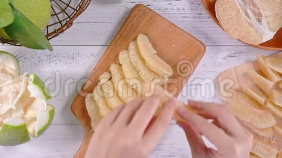 年轻的亚洲妇女正在准备和供应剥皮的新鲜蜜柚在厨房的托盘上明亮的白色木桌顶部的景色超过了视频的预览图