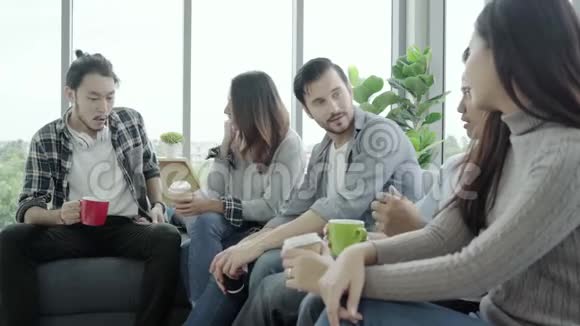 多样化的年轻人团队拿着咖啡杯在办公室坐在沙发上微笑着讨论一些事情视频的预览图
