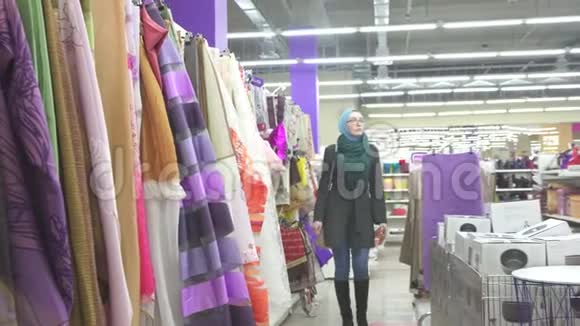 穿着蓝色头巾和眼镜的穆斯林女孩家庭主妇在五金店挑选面料视频的预览图
