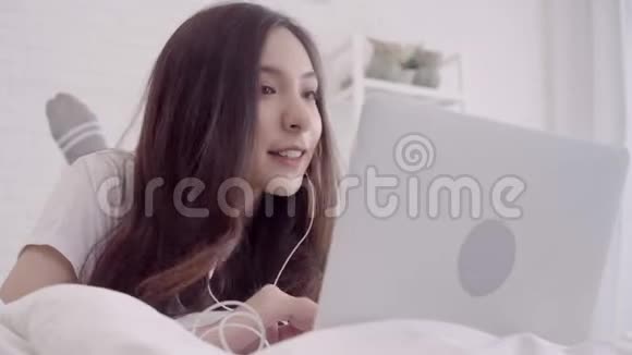 美丽迷人的亚洲女人的肖像使用电脑或笔记本电脑和听音乐躺在床上放松时视频的预览图
