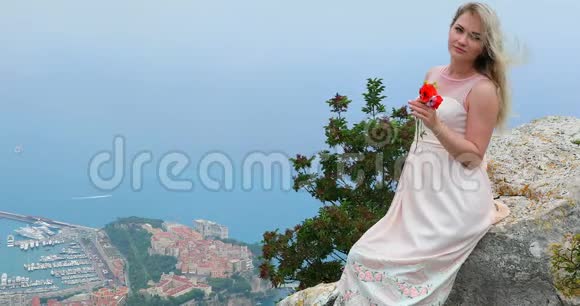 一幅美丽的金发女郎的肖像头发随风飘荡坐在岩石上视频的预览图