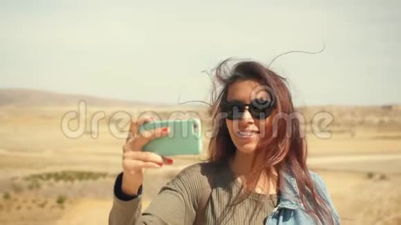 年轻迷人的微笑混合种族女孩在手机上拍摄全景沙漠照片圣诞快乐旅游妇女视频的预览图