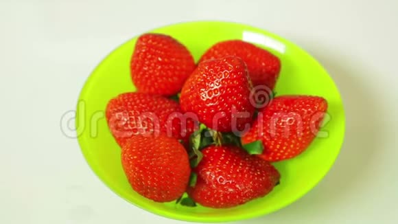 红色的新鲜草莓浆果在绿色的盘子在蓝色的背景旋转成一个圆圈视频的预览图