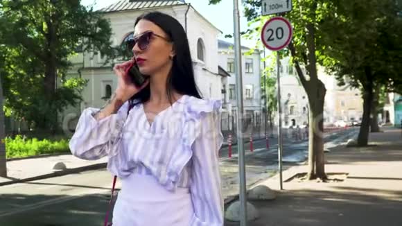 戴墨镜的时髦黑发女人站在城市大街上打电话视频的预览图