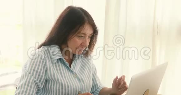 年长的女人欢呼成功的笔记本电脑视频的预览图