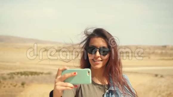 年轻迷人的微笑混合种族女孩在手机上拍摄全景沙漠照片圣诞快乐旅游妇女视频的预览图