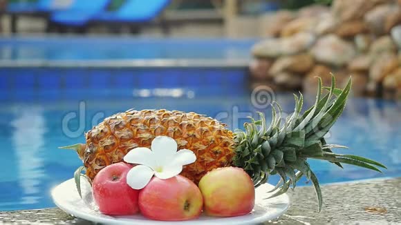 水溅在水果上菠萝玫瑰苹果和弗兰吉帕尼花在游泳池的背面缓慢移动视频的预览图