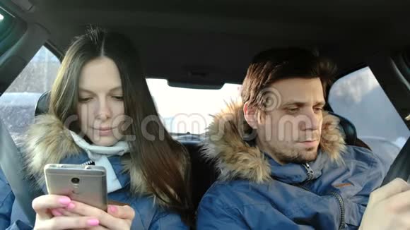 穿着蓝色羽绒服的黑发男人和女人坐在车里看手机里的东西视频的预览图