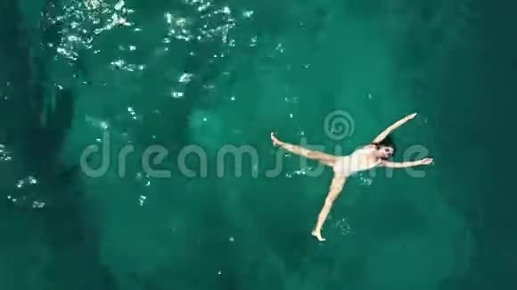一位穿着白色泳衣在海中洗澡的年轻美女的空中自顶向下上升镜头视频的预览图