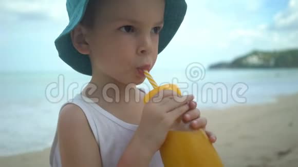 可爱的小男孩在海滩上喝着新鲜的热带芒果奶昔夏季概念视频的预览图