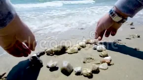 年轻人在海边的海滩上形成一颗有小石头的心视频的预览图