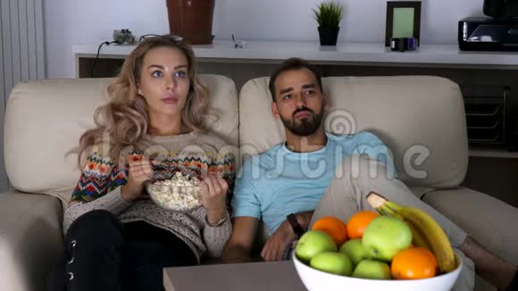 一对夫妇在客厅的沙发上晚上看恐怖电影视频的预览图
