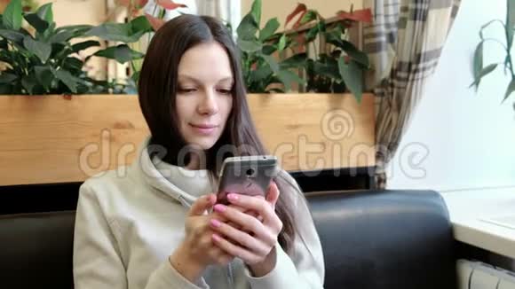 快乐的年轻黑发女人正在考虑一些有趣的事情在咖啡馆里玩手机视频的预览图