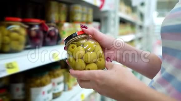 接近白种人的女人手靠近商店货架在杂货店里选择腌菜绿橄榄视频的预览图