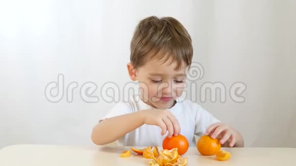 男孩玩橘子特写在白色背景一个快乐的孩子双手坐在桌子旁视频的预览图