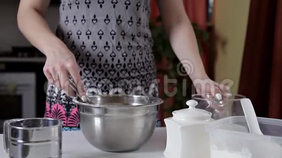 一个女人把杯子里的牛奶倒入有面团的碗里女孩准备煎饼饼干面团视频的预览图