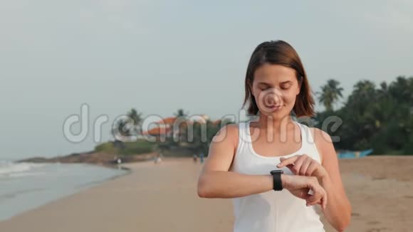 活跃的生活方式女性游客看科技智能手表特写宏观特写手臂海滩触摸屏上视频的预览图