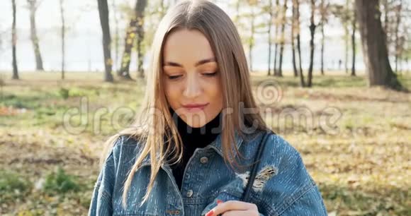 年轻迷人的女性的肖像她微笑着看着秋天公园的相机开心的漂亮女人视频的预览图