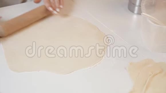 一位女面包师用擀面杖在木桌和面粉上的配料背景下擀出面团视频的预览图